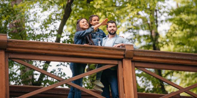 Happy interracial family standing on wooden bridge, while mother pointing somewhere