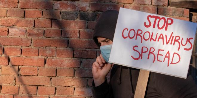 A man in a face mask carrying a sign that reads stop coronavirus spread.